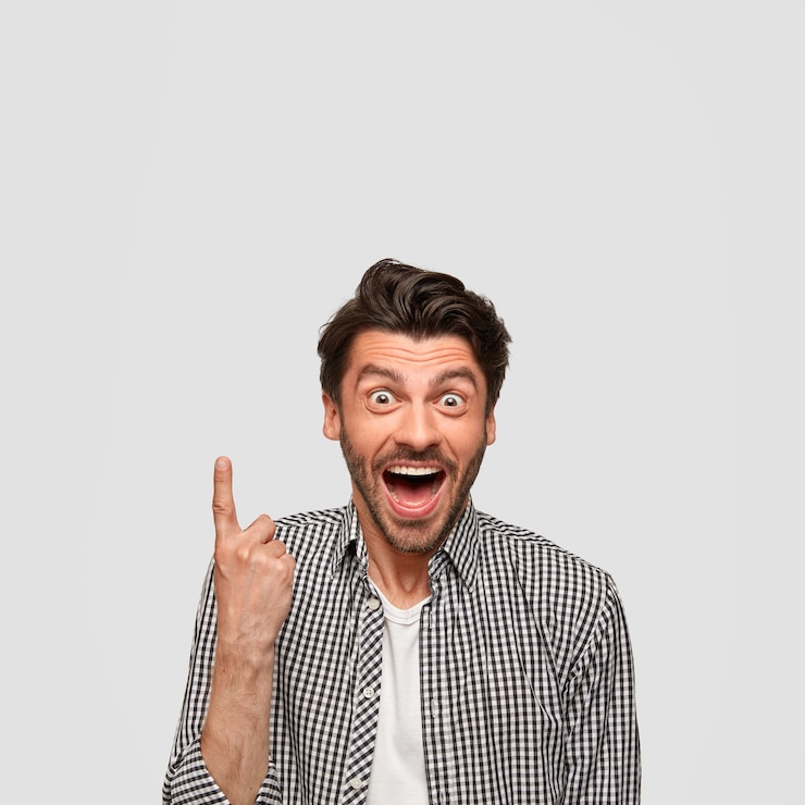 Foto grátis imagem de um jovem branco alegre e feliz com expressão de surpresa, aponta para cima e o encara com olhos esbugalhados