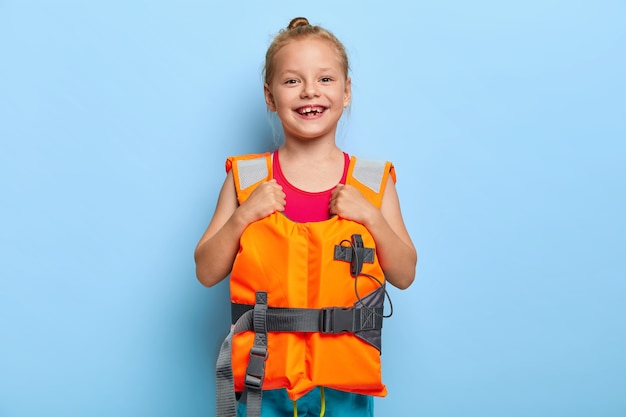 Imagem de uma adorável menina ruiva usando colete salva-vidas protetor, aproveitando as férias de verão em segurança, estação do ano favorita