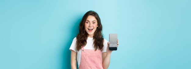 Imagem de uma bela jovem parece surpresa e animada mostrando a tela vazia do smartphone seu logotipo