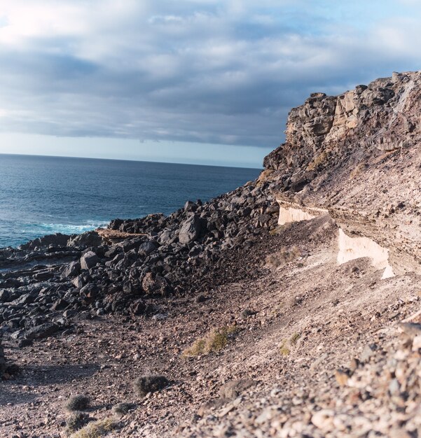 Imagem de uma encosta rochosa ao longo de uma costa marítima sob céu nublado