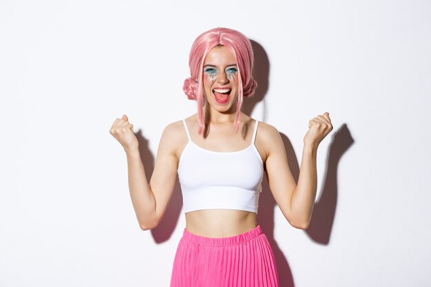Imagem de uma garota animada e bem-sucedida com uma peruca rosa, comemorando algo, fazendo um soco em punho e sorrindo satisfeita