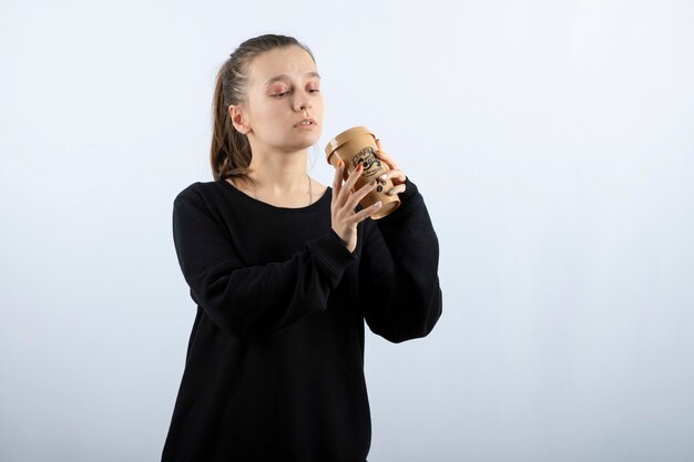 Imagem de uma jovem modelo em pé, bebendo uma xícara de café