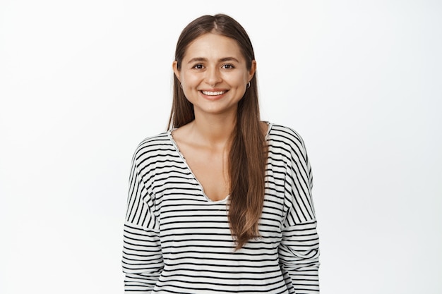 Imagem de uma jovem mulher moderna em seus 30 anos, sorrindo e olhando a expressão do rosto feliz, confiante e esperançosa, em pé sobre branco.