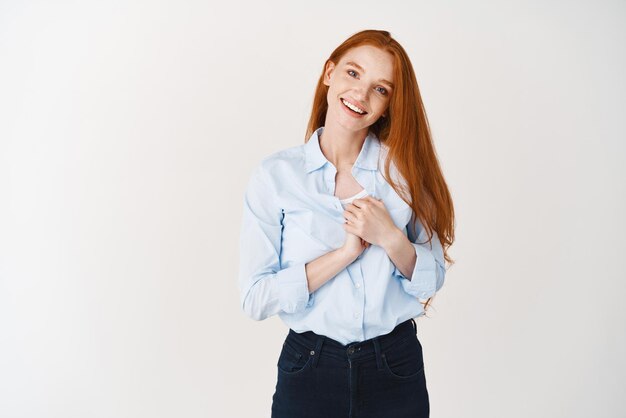 Imagem de uma jovem ruiva sendo grata de mãos dadas perto do coração e sorrindo agradecendo a você em pé de coração contra o fundo branco