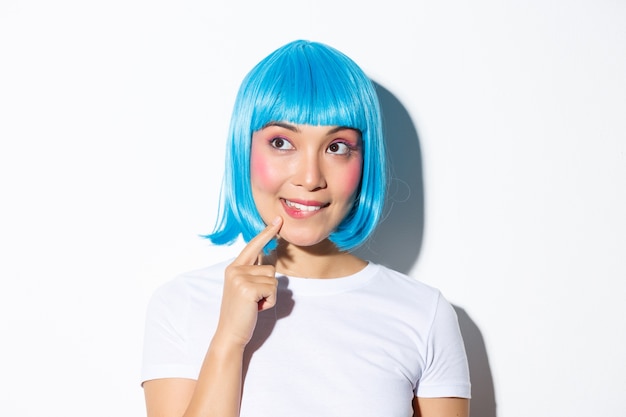 Imagem de uma linda garota asiática pensativa na peruca azul, olhando para o canto superior esquerdo e pensando, em pé.