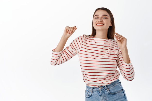 Foto grátis imagem de uma linda garota curtindo um bom dia, dançando e se divertindo, sorrindo com uma expressão positiva e feliz, posando despreocupada em roupa casual contra um fundo branco