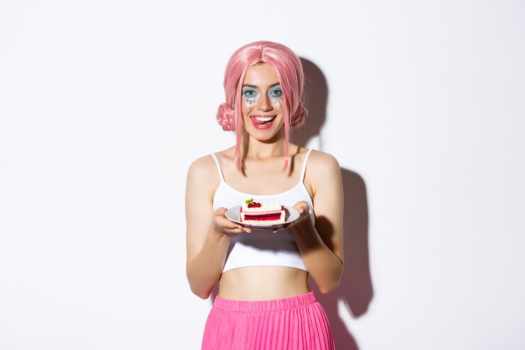Foto grátis imagem de uma linda garota na peruca rosa, lambendo os lábios, segurando um bolo saboroso, comemorando algo, em pé.