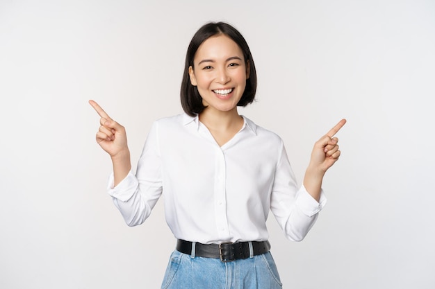 Imagem de uma linda mulher asiática apontando os dedos para a esquerda e para a direita tomando decisão mostrando duas opções de variantes sobre fundo branco
