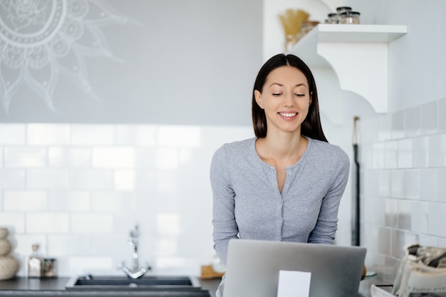 Foto grátis imagem de uma linda mulher morena sentada na mesa da cozinha e usando o laptop