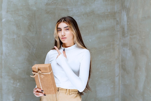 Imagem de uma modelo de menina com um presente de papel apontando para longe sobre uma pedra