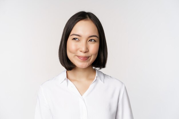 Imagem de uma mulher asiática sorridente planejando pensar em sonhar acordado em pé sobre fundo branco com rosto presunçoso