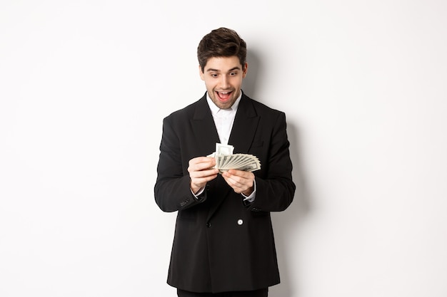 Imagem do empresário bonito animado, contando dinheiro e sorrindo divertido, de pé contra um fundo branco no terno.