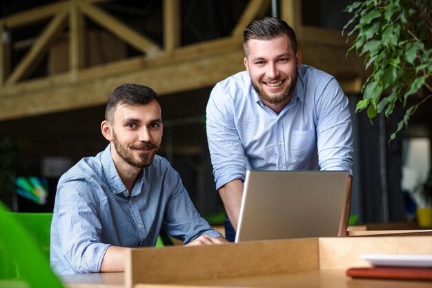 Imagem do empresário bonito ouvindo seu colega ou parceiro sobre o sistema de negócios ner enquanto trabalhava no computador portátil no interior do escritório