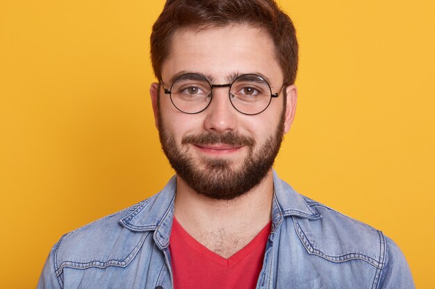 Imagem horizontal interior de jovem bonito feliz olhando diretamente sorrindo sinceramente, usando óculos