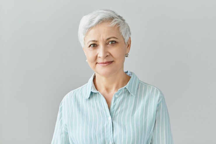 Foto grátis imagem isolada de uma mulher de negócios europeia simpática e bonita, com cabelo grisalho e sorrindo com confiança, feliz com os resultados do trabalho de sua equipe, vestida com uma camisa formal listrada