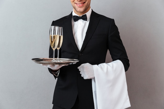 Imagem recortada de garçom segurando copos de champanhe e toalha.