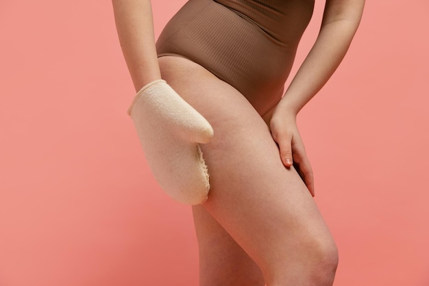 Imagem recortada de mulher de pernas femininas fazendo massagem com luvas especiais isoladas sobre fundo rosa