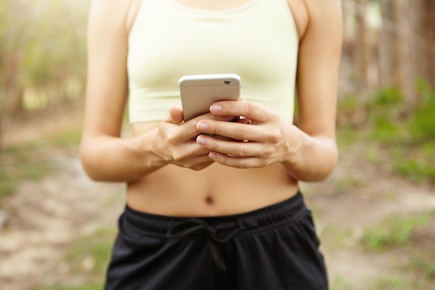 Imagem recortada de mulher treinando ao ar livre e rastreando sua rota de aptidão no celular.