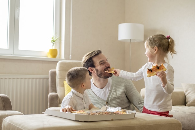 Imagem superficial de um pai caucasiano comendo pizza e se divertindo com os filhos