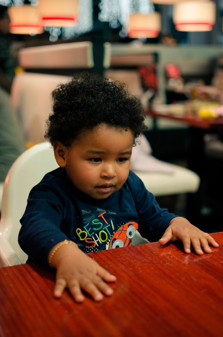 Foto grátis imagem vertical com foco superficial de um bebê afro-americano sentado em uma cadeira alta