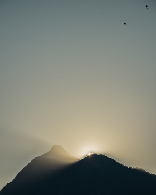 Imagem vertical das silhuetas de colinas sob a luz do sol durante o pôr do sol