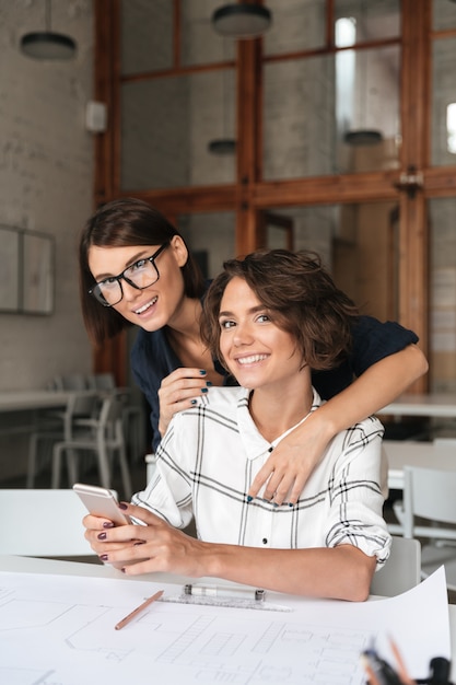 Imagem vertical de duas jovens mulheres felizes usando smartphone