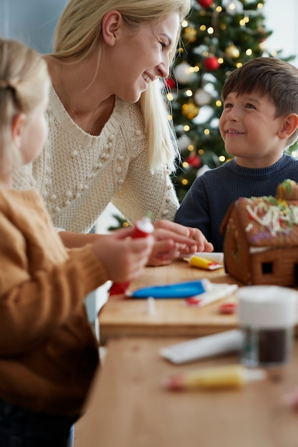 Imagem vertical de família decorando casa de pão de gengibre