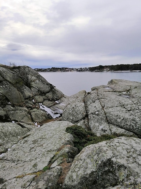 Imagem vertical de rochas cercadas pelo rio sob um céu nublado na Noruega