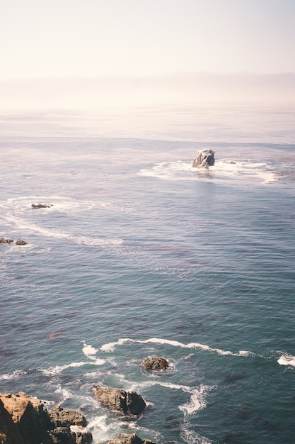 Imagem vertical de rochas no oceano perto da costa de um penhasco
