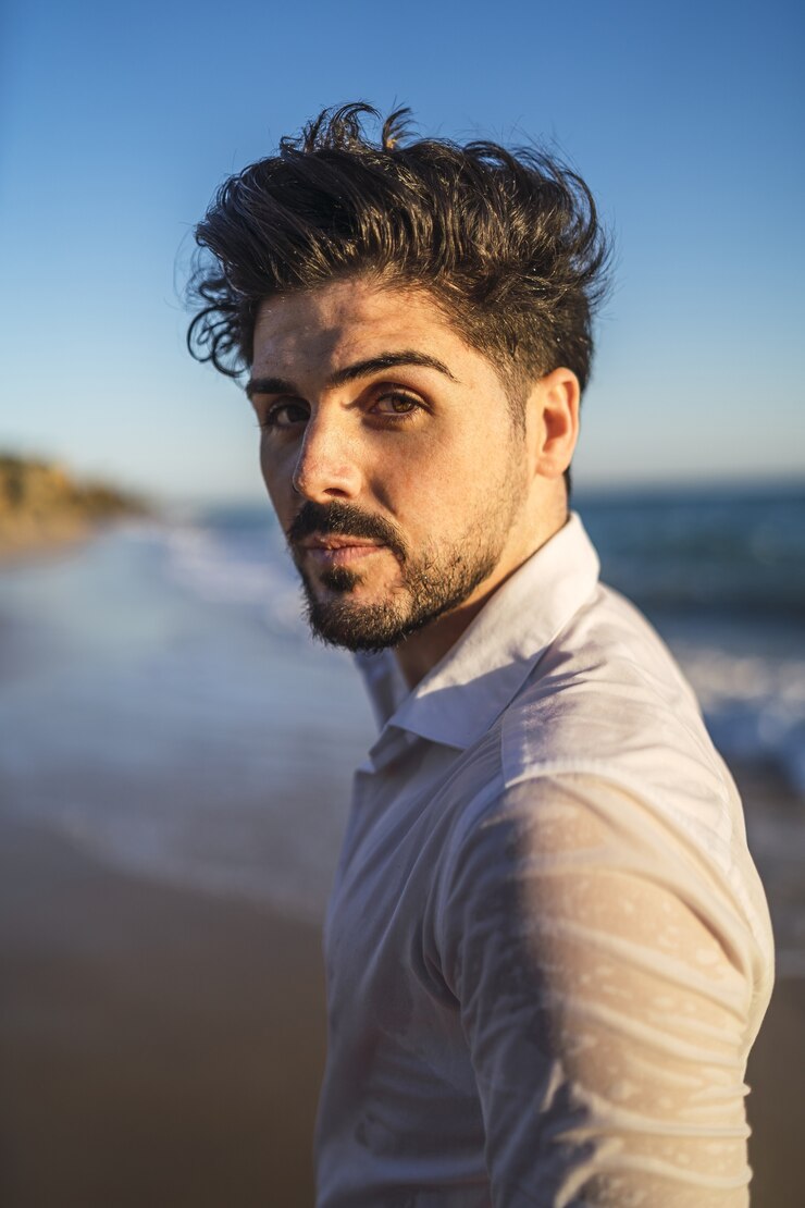 Foto grátis imagem vertical de um homem moreno em uma camisa branca contra um oceano