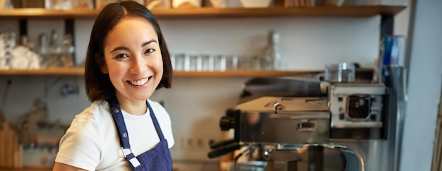 Foto grátis imagem vertical de uma barista amigável sorrindo para você enquanto prepara café, derramando leite e fazendo