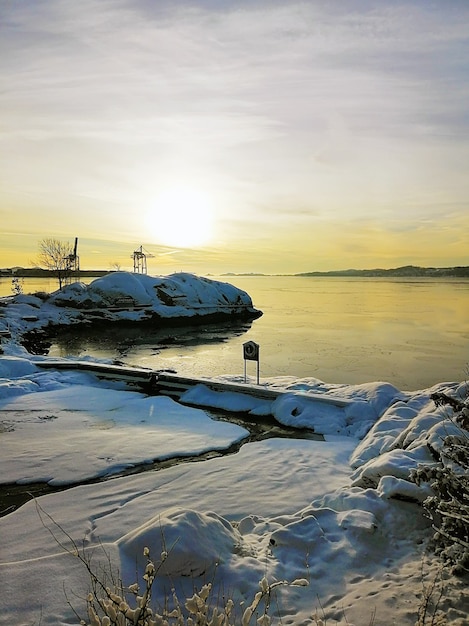 Imagem vertical de uma ilha coberta de neve rodeada pelo mar durante o pôr do sol na Noruega