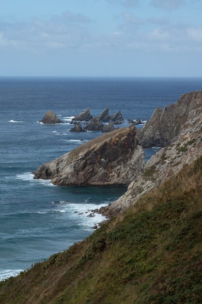 Imagem vertical do mar cercado por rochas cobertas de musgos sob um céu nublado