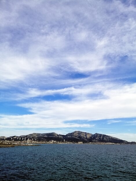 Imagem vertical do mar cercado por rochas sob um céu nublado em Marselha, na França