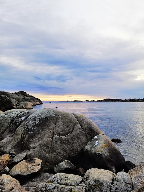 Imagem vertical do mar rodeado por rochas sob um céu nublado durante o pôr do sol na Noruega