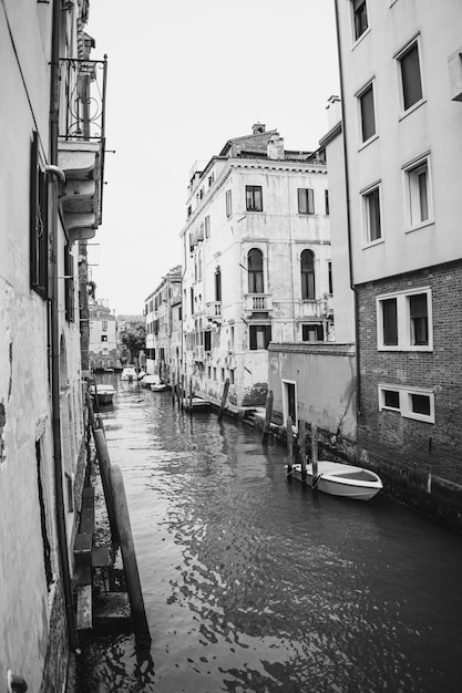 Imagem vertical em tons de cinza de um canal com barcos e edifícios antigos em veneza, itália