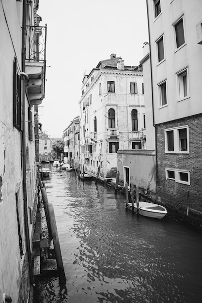 Imagem vertical em tons de cinza de um canal com barcos e edifícios antigos em Veneza, Itália