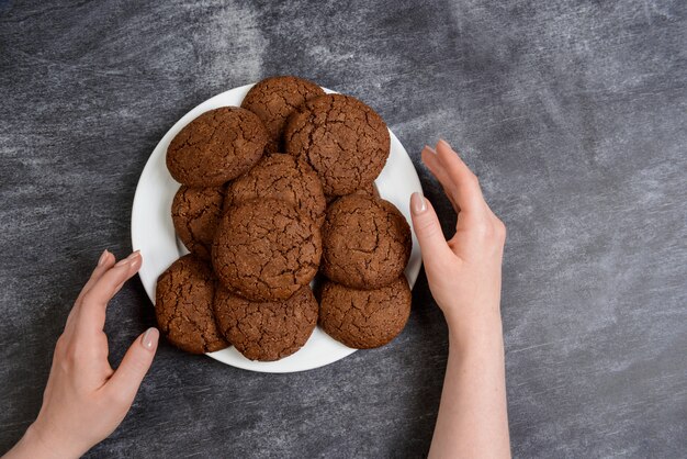 Imagens de mãos segurando biscoitos de chocolate sobre a superfície de madeira