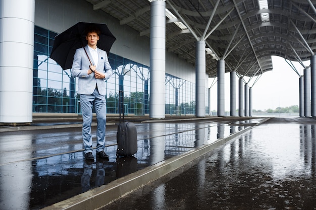 Imagens do empresário ruivo jovem confiante segurando guarda-chuva preta na chuva no aeroporto