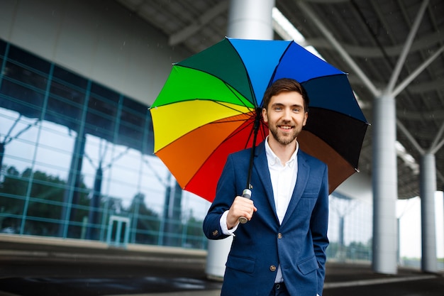 Imagens do jovem empresário alegre segurando guarda-chuva heterogêneo na rua chuvosa