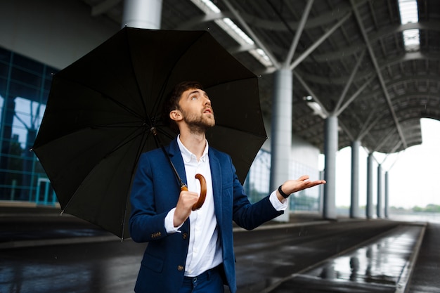 Imagens do jovem empresário segurando guarda-chuva na chuva, olhando para as gotas