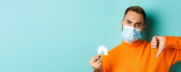 Imobiliário e conceito de pandemia de coronavírus fechado de homem desapontado com máscara facial mostrando pequeno