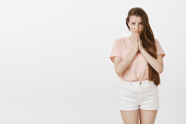 Implorando uma linda garota adolescente posando contra a parede branca