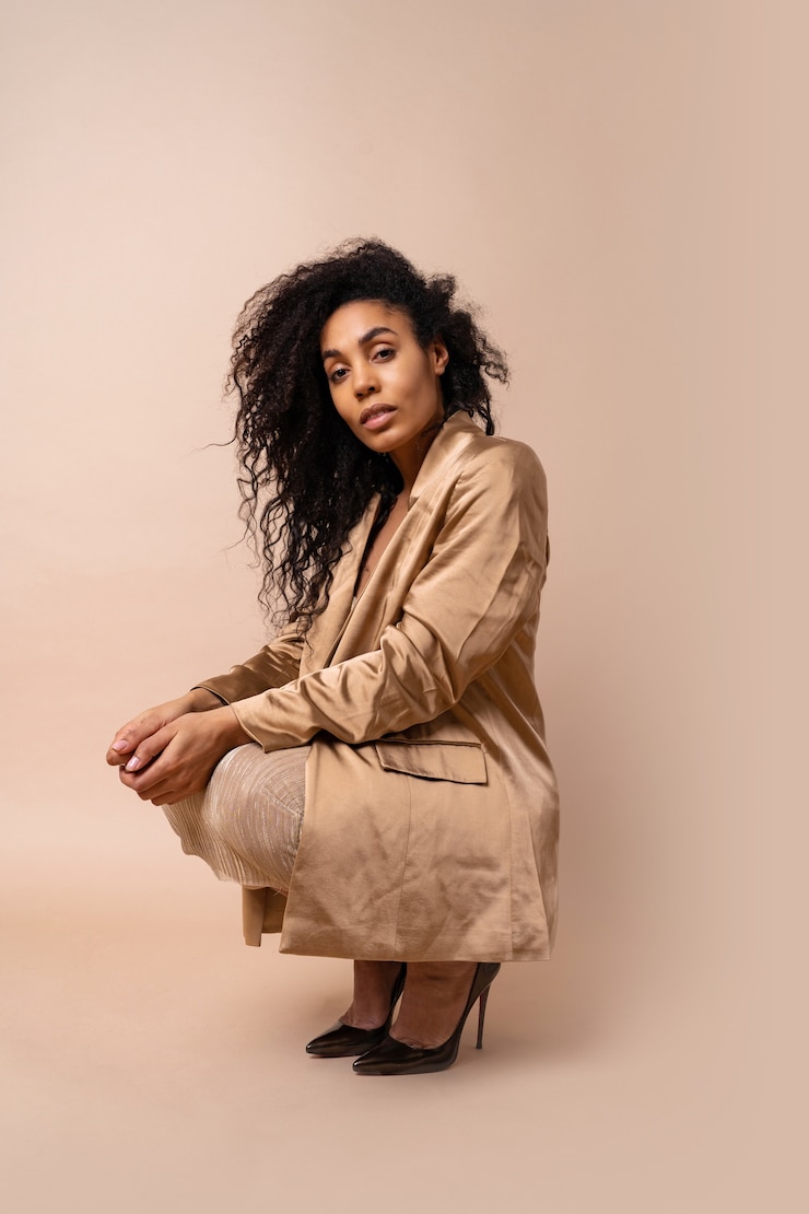Foto grátis impressionante modelo bronzeado com penteado encaracolado volumoso em vestido dourado brilhante e blazer de cetim posando.