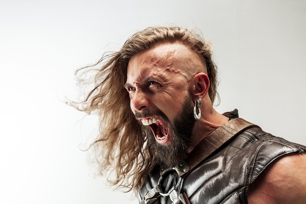 Incontrolável. cabelo comprido loiro e modelo masculino musculoso em traje de couro de viking com o grande martelo cosplay isolado no fundo branco do estúdio. guerreiro da fantasia, conceito de batalha antigo.