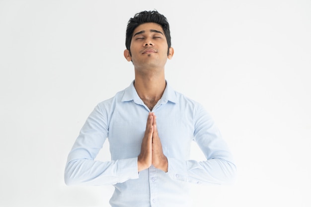 Indivíduo indiano sereno na camisa branca que praying com olhos fechados.