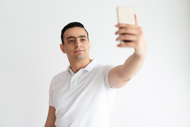 Indivíduo novo de sorriso que toma a foto do selfie no smartphone. homem indiano usando dispositivo digital.