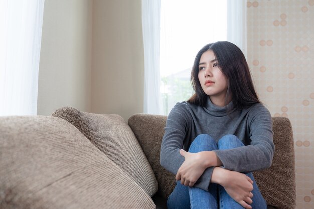 Infeliz mulher jovem e bonita asiática localização sozinha no sofá com sentimento de tristeza