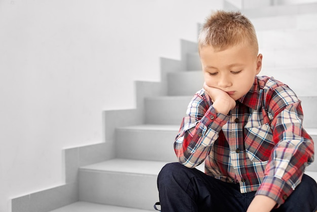 Infelizmente menino de escola nas escadas no corredor da escola e chorando