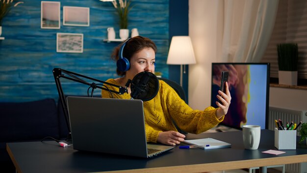 Influenciador com fones de ouvido usando telefone para tirar séries de podcast de gravação de selfie para o público. Produção on-line on-line, transmissão de show pela Internet, host de streaming de conteúdo ao vivo para mídia social digital